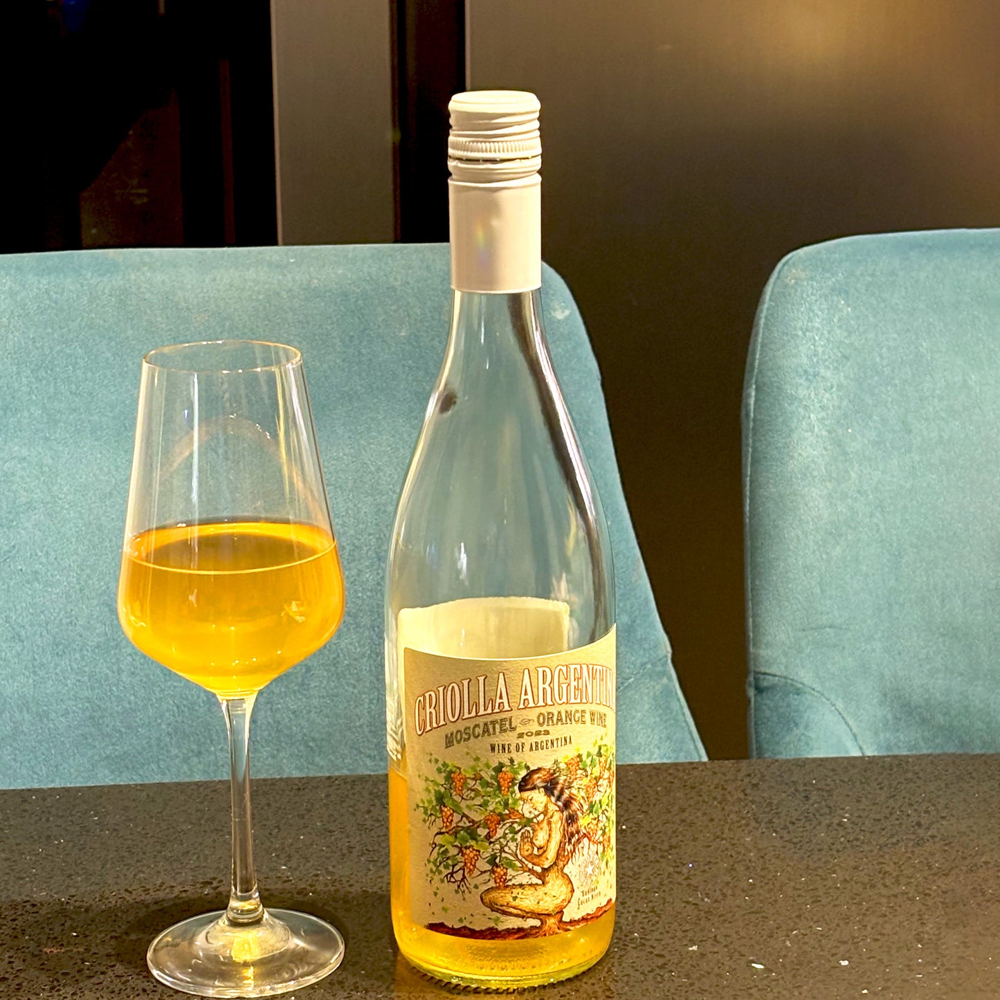 Criolla Wines Moscatel Orange poured into a glass on a kitchen granite countertop contrasting with bright blue barstools