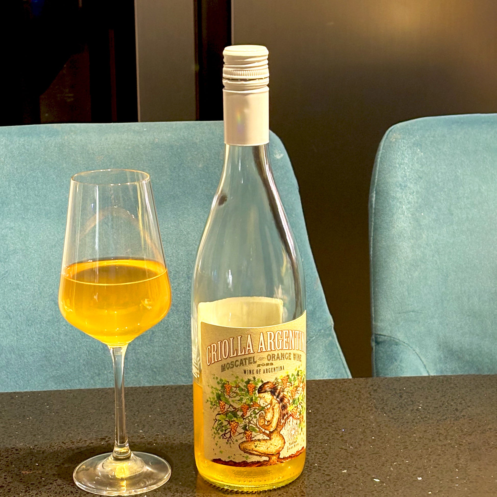 Criolla Wines Moscatel Orange poured into a glass on a kitchen granite countertop contrasting with bright blue barstools