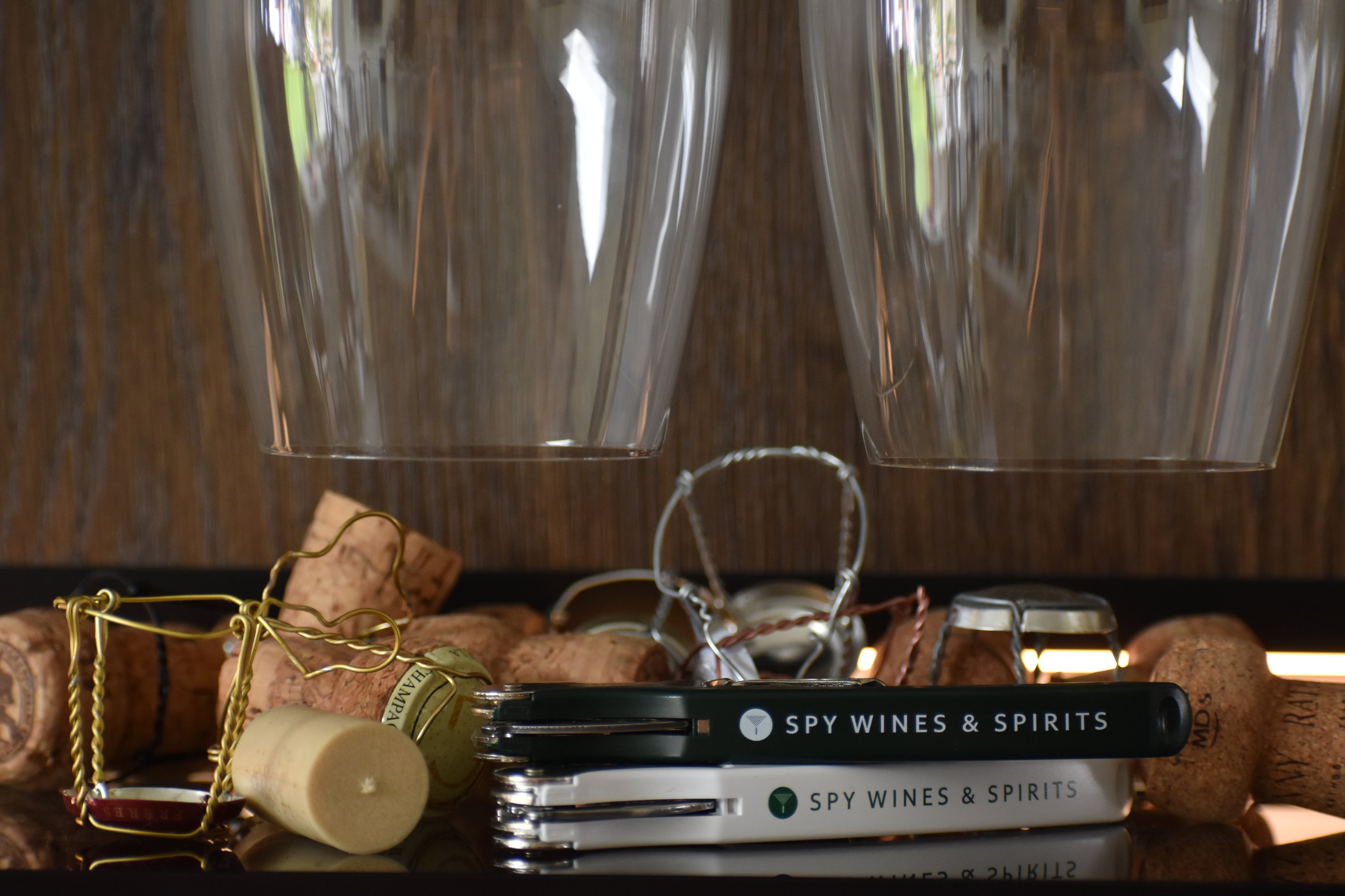 Two wine glasses, corks, and a Spy Wines & Spirits corkscrew on a wooden surface.