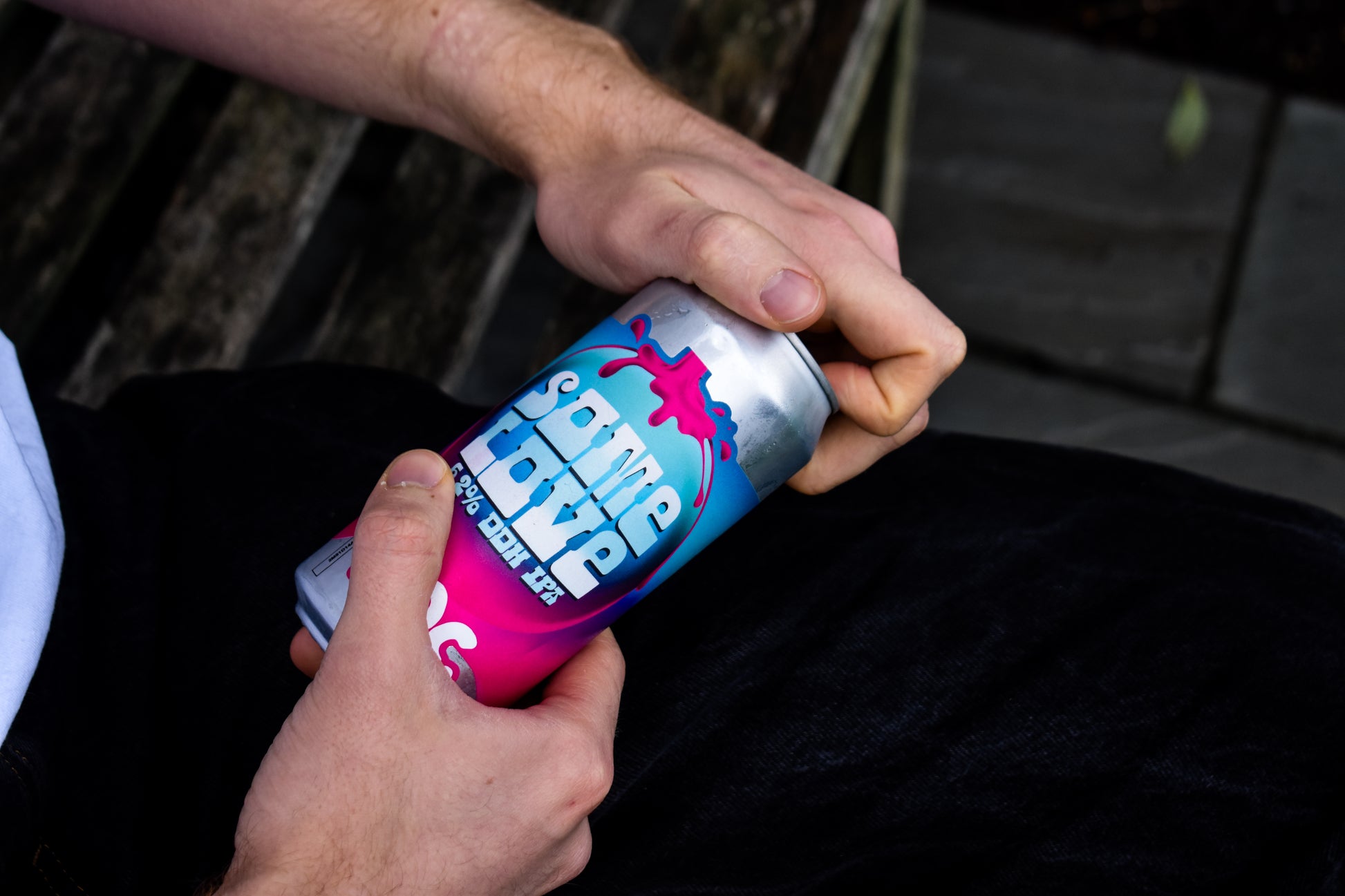 Man holding pink and blue can at angle on a bench