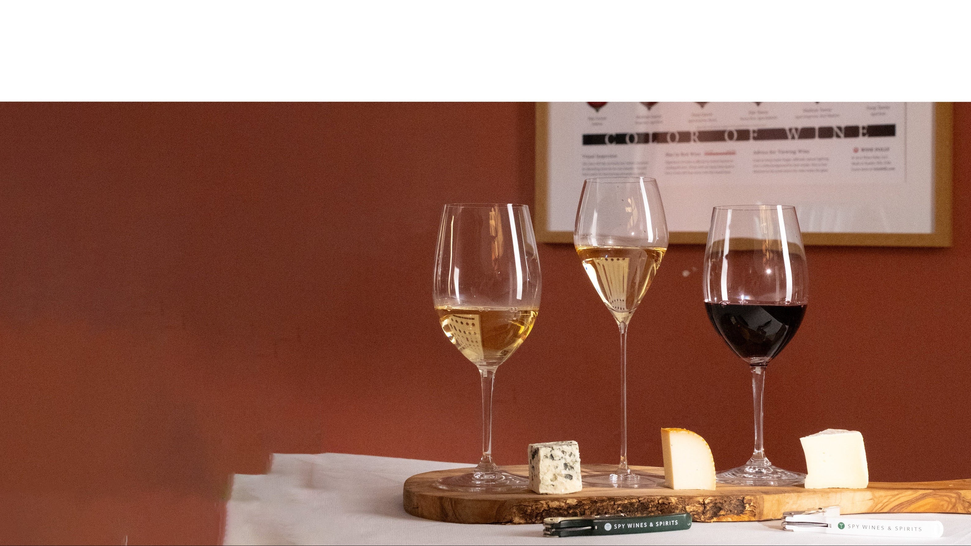 3 glasses of wine paired with cheese on board with red background