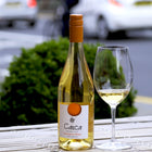 Bottle of Orange French wine poured in a glass on a table outside in front of a green bush