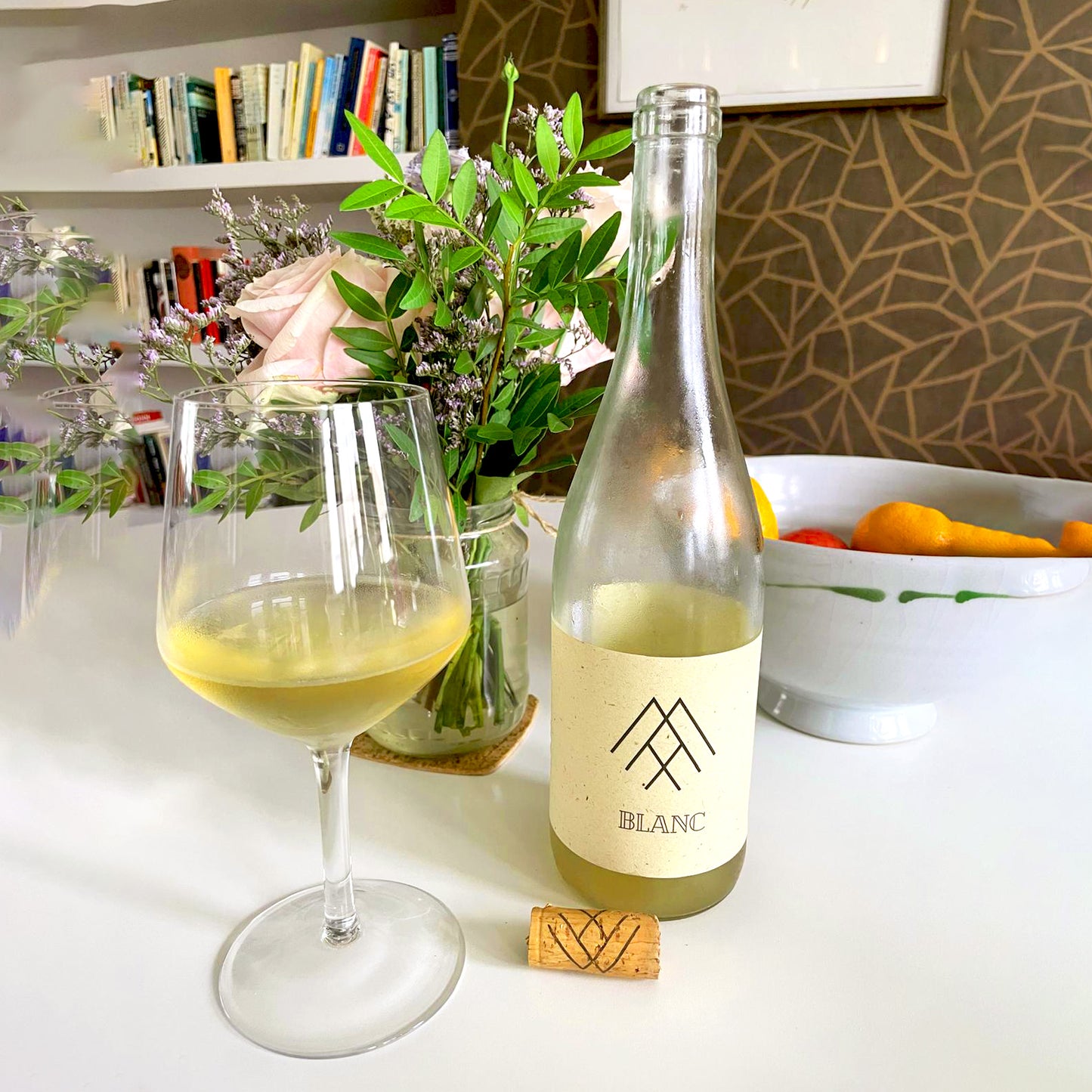 Max Sein Wein Blanc Wine Bottle Lifestyle Shot with a glass full of wine, flowers and a kitchen setting